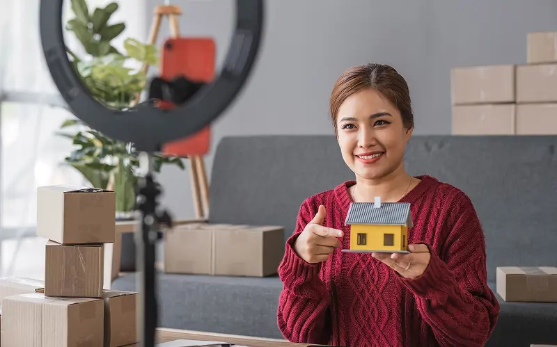 A women is holding a dummy home infront of camera to do marketing.